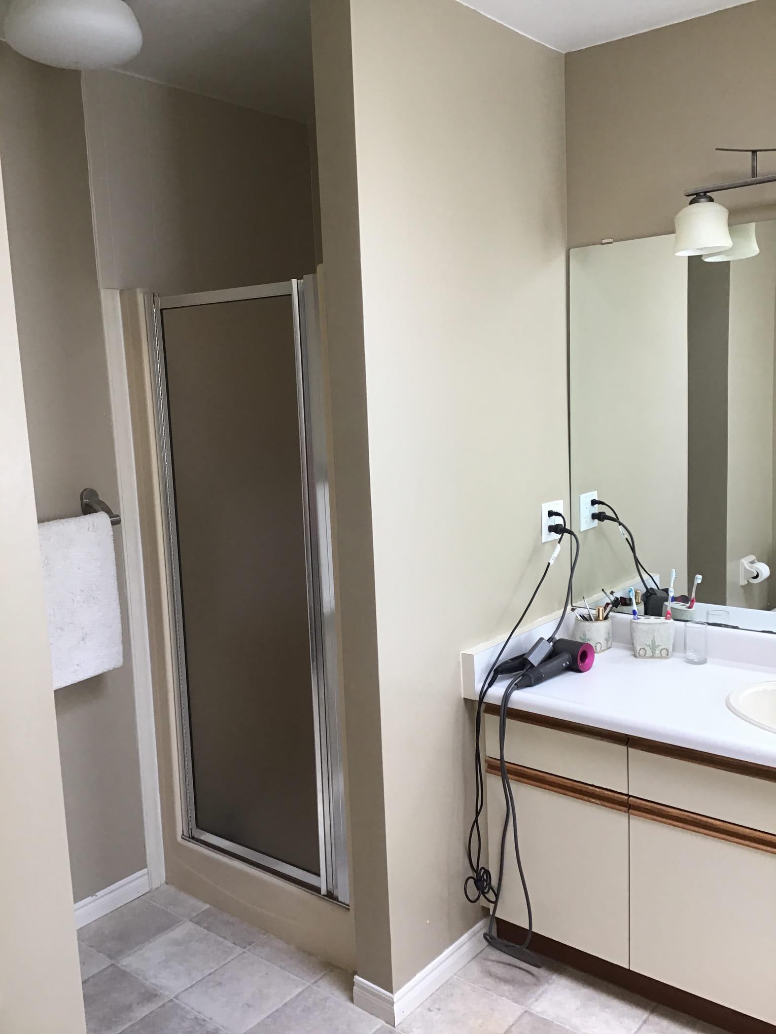 bathroom-renovation-london-ontario-donaldson.jpg Bathroom with a shower stall on the left, a vanity with a mirror, hairdryer, and toiletries on the right.
