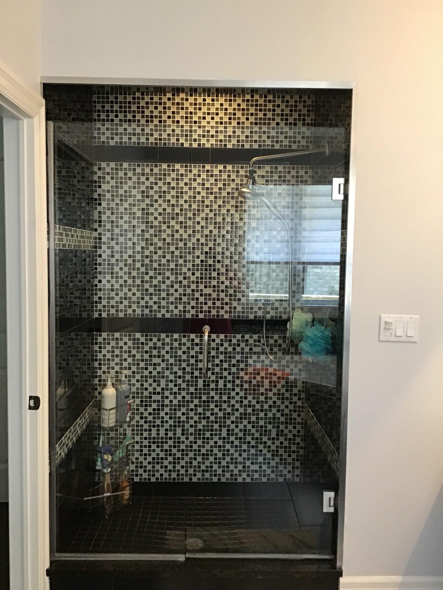 bathroom-renovation-london-ontario-donaldson.jpg Walk-in shower with glass enclosure, black and white mosaic tiles, dark floor, and shower caddy.