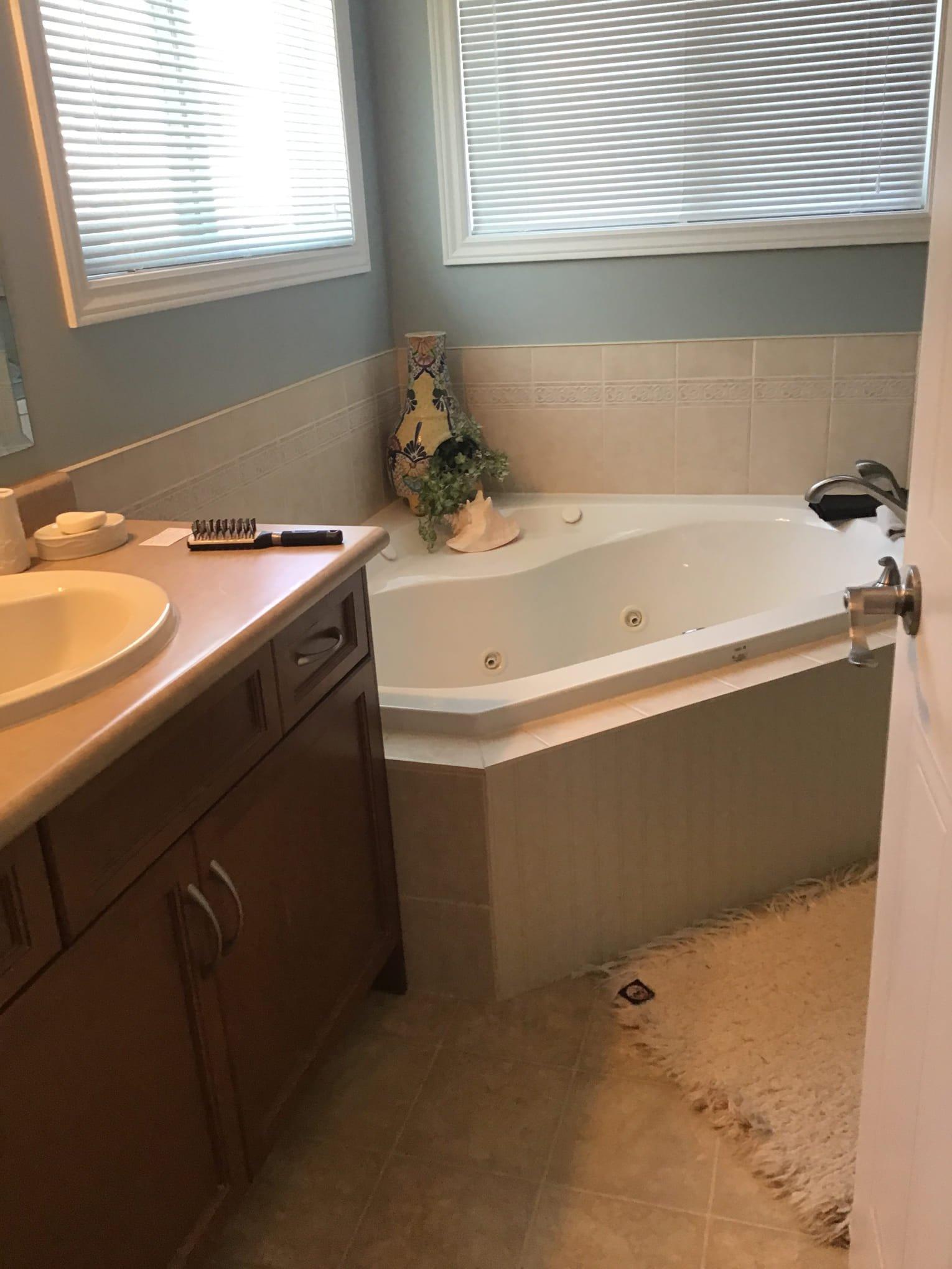 bathroom-renovation-london-ontario-donaldson.jpg A bathroom featuring a white corner jetted tub, a brown vanity with a sink, and two windows with white blinds.