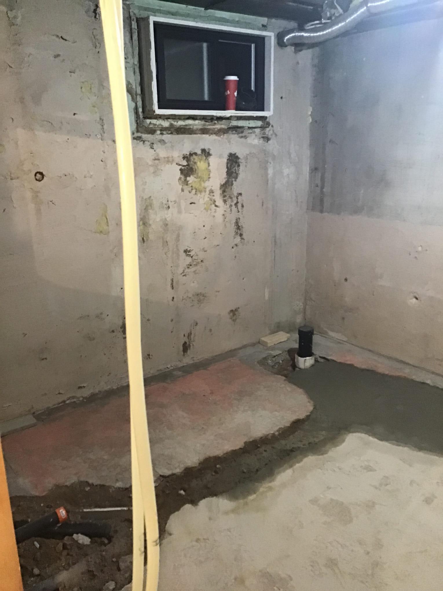 bathroom-renovation-london-ontario-donaldson.jpg Unfinished concrete basement with stained walls, a small window holding a red cup, exposed ductwork, and a partial dirt floor with a drain pipe.