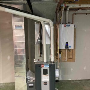 Trane installed furnace in basement with tankless water heater mounted on wall behind.