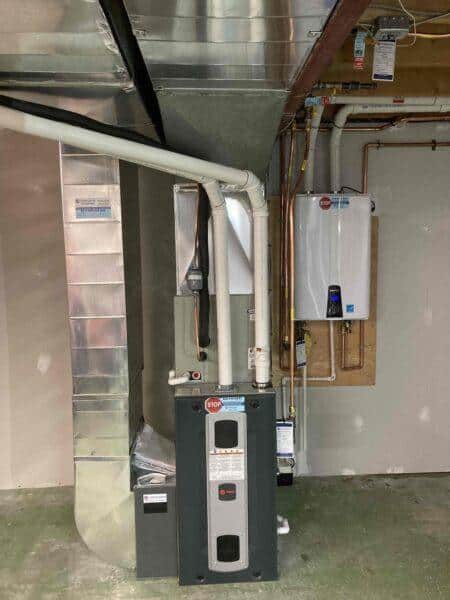 Trane installed furnace in basement with tankless water heater mounted on wall behind.